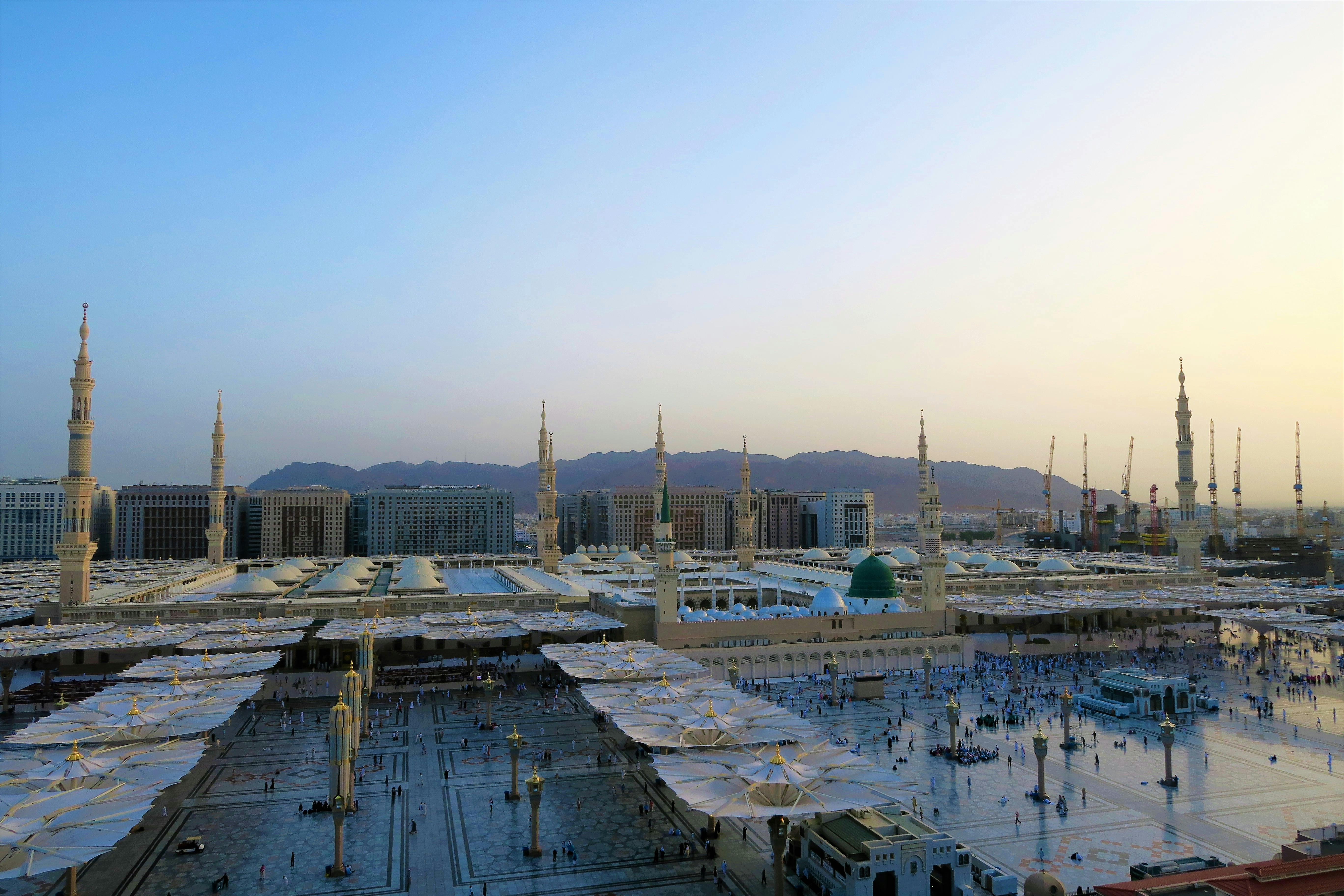 A grand and serene view of the Masjid Al Haram, with the Kaaba at its heart, bustling with pilgrims under a clear sky.